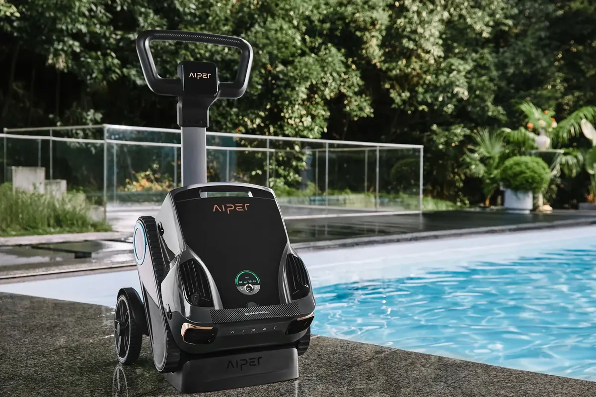 Aiper Scuba X1 Pro Max cordless robotic pool cleaner sitting on its wheeled caddy and wireless charging dock beside a pool