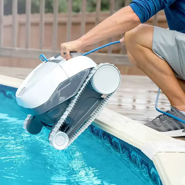 A person lifting a Dolphin E10 robot out of a pool by its handle, water draining from it