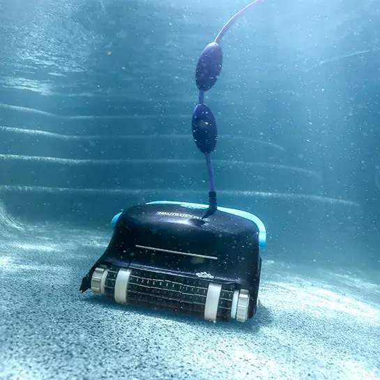 Dolphin Nautilus CC Plus scrubbing a pebble pool floor underwater, its floating blue cable rising to the surface